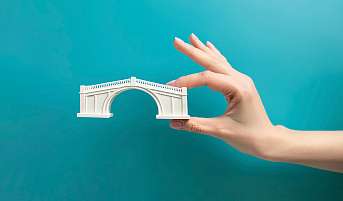 Eine Hand hält eine Brücke in der Hand. Symbolisch für die Überbrückung 