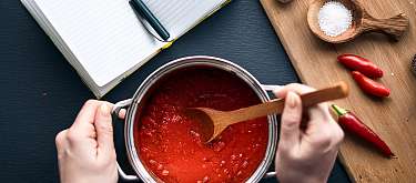 Auftragsentwicklung MALIAN Manufaktur Hände kochen Sauce, daneben liegt ein Notizbuch. Symbolisch für: Entwicklung von Rezepten für Unternhemen im Gastro-Bereich