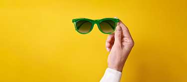 Eine Hand, die eine grüne Sonnenbrille hält.
