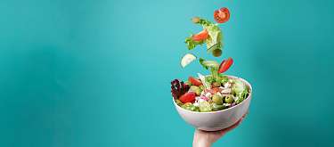 Eine Hand die ein Schüsselchen voller Salat hochhält.