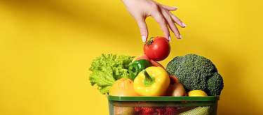Aktiv gegen Food Waste Eine Hand nimmt eine gute Tomate aus einem Abfallkorb voller toller Früchte und Gemüse. Symbolisch für: Wir bewahren Lebensmittel vor der Tonne.