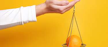 Rohstoff-orientiert Eine Hand hält eine Wage mit einer Frucht. Symbolisch für Abwägen rohstoff-orienterte gegen produktorientierte Herstellung