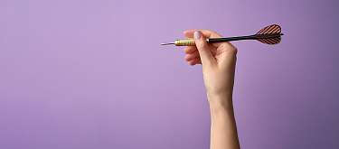 Eine Hand die einen Dartpfeil hochhält. Symbole fürs Zielen